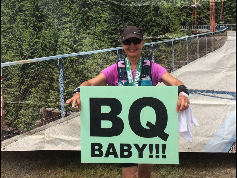 Womans at the end of a marathon finish line, holding a 'BQ Baby' sign